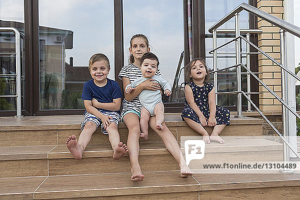 Portrait barefoot brothers and sisters sitting on patio steps