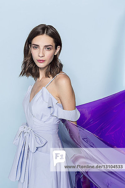 Portrait of a female fashion model posing with purple plastic sheet against blue background