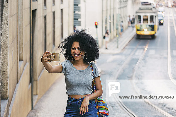 Young woman with smart phone taking selfie on urban street