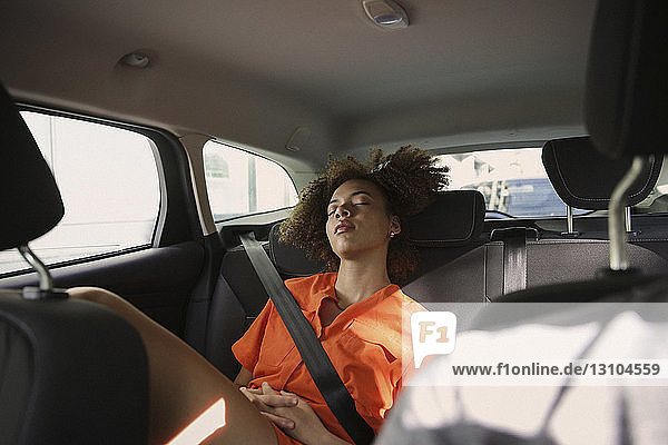 Müde junge Frau schläft auf dem Rücksitz eines Autos
