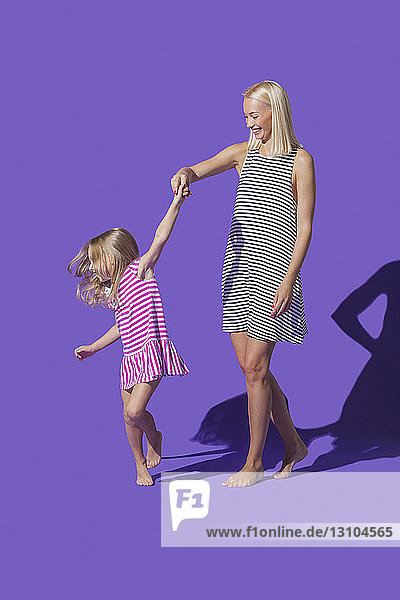 Mother and daughter in striped dresses dancing on purple background