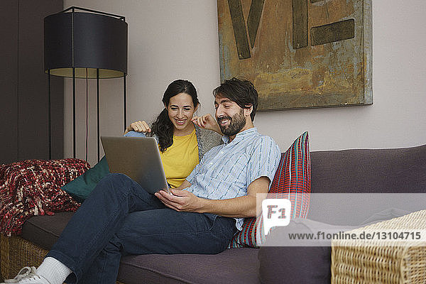 Couple using laptop on living room sofa