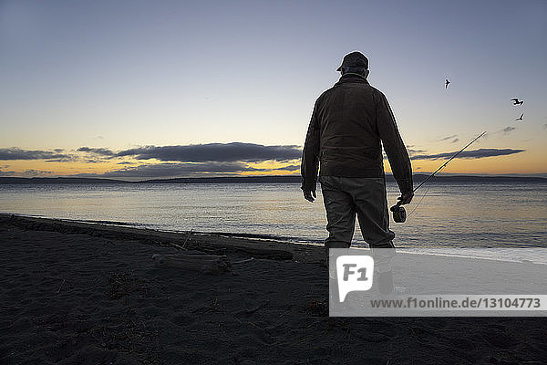 A fly fisherman gets ready to wade into salt water at sunrise and fly fish for coastal cutthroat trout and salmon at a beach on the north west coastline of the USA.