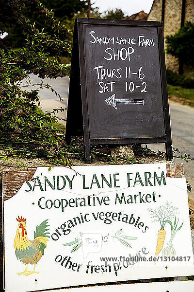 Nahaufnahme des Schildes und der Tafel mit den Öffnungszeiten des Hofladens Sandy Lane.