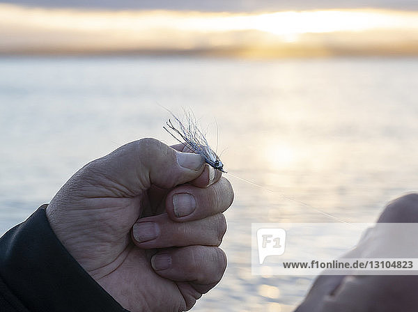 Nahaufnahme eines Fliegenfischers  der eine neue Fliege an seine Schnur bindet  in der Erwartung  eine weitere Forelle oder einen Lachs im Salzwasser zu fangen.