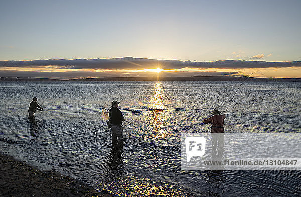 Two fly fishermen cast for searun coastal cutthroat trout and salmon at sunrise with their guide standing between them at the salt water beach at a beach on the north west coastline of the USA.