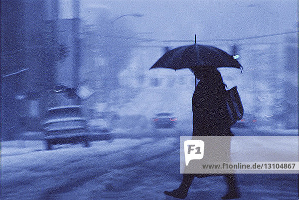 Eine Frau  die über eine Straße der Stadt geht  die im Winter von Schnee und Regen bedeckt ist.