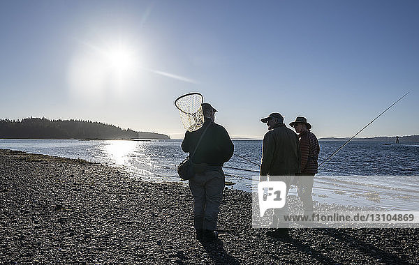 Zwei Fliegenfischer sprechen mit ihrem Führer über neue Techniken beim Fliegenfischen auf Cutthroat-Forellen an einem Strand an der Nordwestküste der USA.
