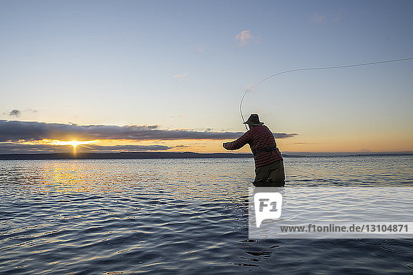 Die Silhouettenansicht eines Fliegenfischers  der an einem Strand an der Nordwestküste der USA von einem Salzwasserstrand aus nach Lachsen und Cutthroat-Forellen der Searun-Küste wirft.