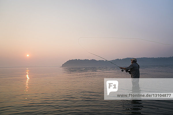 Hochrangige kaukasische männliche Fliegenfischerei auf Lachs und Cutthroat-Forellen vor der Küste