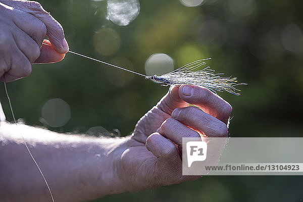 Nahaufnahme eines Fliegenfischers  der eine neue gefiederte Angelfliege an seine Schnur bindet  um sie im Salzwasser zu verwenden.