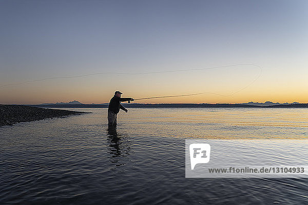A silhouette view of a fly fisherman casting for salmon and searun coastal cutthroat trout from a salt water beach at a beach on the north west coastline of the USA.