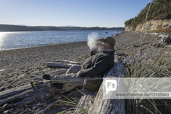 A fly fisherman enjoys a cigar and takes a break from fly fishing for searun coastal cutthroat trout and salmon in northwest Washington State USA