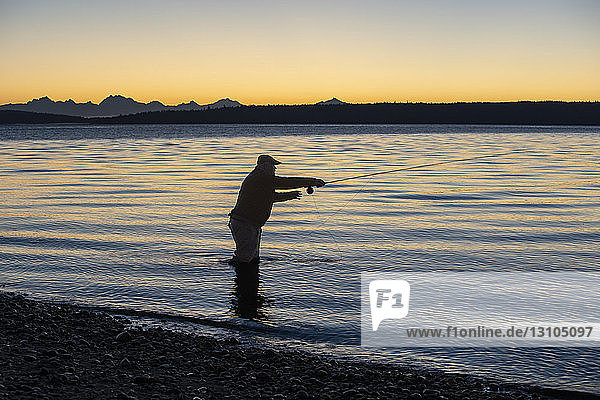 Die Silhouette eines Fliegenfischers  der bei Sonnenaufgang an einem Strand an der Westküste der USA nach Cutthroat-Forellen wirft