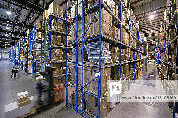 Overview of a large industrial distribution warehouse storing products in cardboard boxes on conveyor belts and racks.