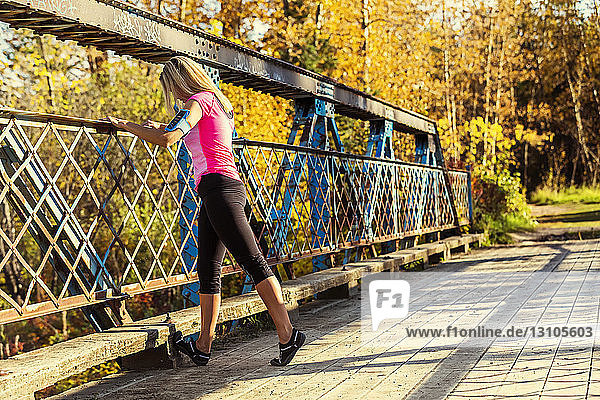 An attractive middle-aged woman pauses to rest on a bridge during a run on a beautiful warm fall evening in a city park; Edmonton  Alberta  Canada