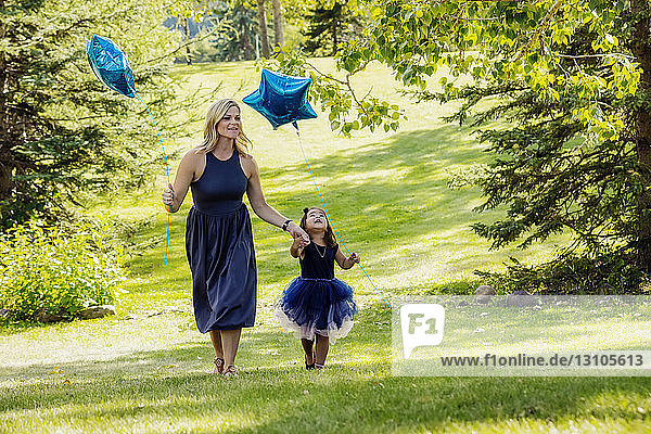 A mother walking through a park on a warm fall day with her little girl who is wearing a party dress and they are both carrying star shaped balloons; Edmonton  Alberta  Canada