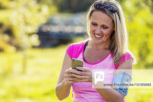 A mature woman wearing active wear and an arm band to hold her smart phone texts before heading out for a run in a city park during the fall season; Edmonton  Alberta  Canada
