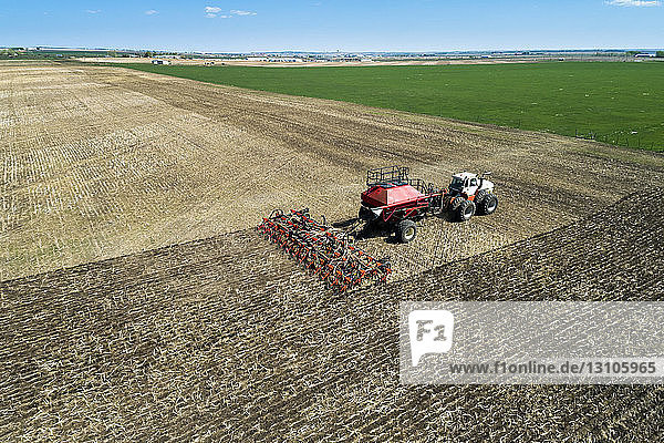 Tractor pulling an air seeder  seeding a field with blue sky in the distance  West of High River; Alberta  Canada