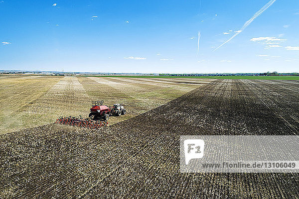 Tractor pulling an air seeder  seeding a field with blue sky in the distance  West of High River; Alberta  Canada