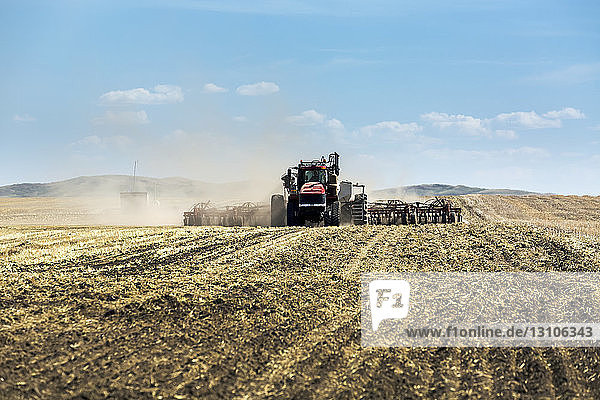 Traktor,  der eine pneumatische Sämaschine zieht und ein Feld mit blauem Himmel und Wolken im Hintergrund sät; Rockyford,  Alberta,  Kanada