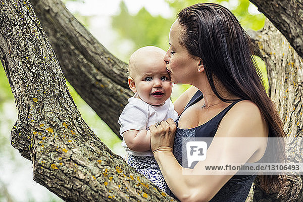 A young mother kissing her distressed infant daughter in a park; Edmonton  Alberta  Canada