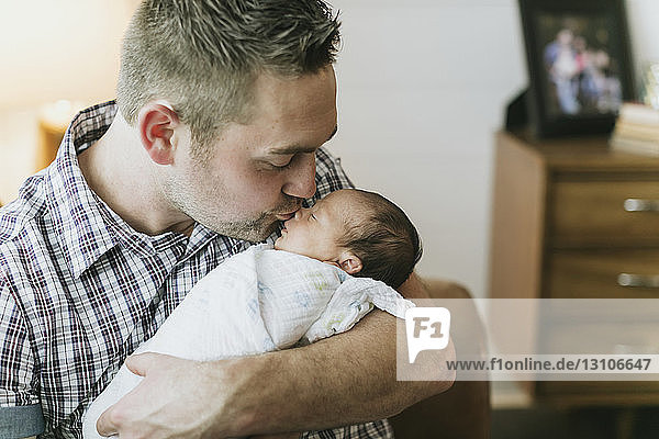 Portrait of a father holding and kissing his newborn baby; Surrey  British Columbia  Canada