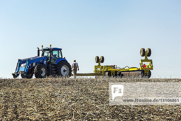 Farmer walking towards tractor with rollers in a canola stubble field with blue sky; Acme  Alberta  Canada