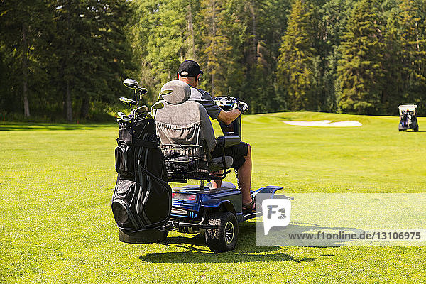 A physically disabled golfer driving a specialized golf wheelchair between holes on a golf course during a tournament; Edmonton  Alberta  Canada