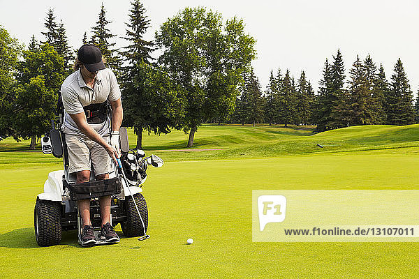 Ein körperlich behinderter Golfer  der einen Ball auf ein Golfgrün schlägt und einen speziellen motorisierten Hydraulikrollstuhl zur Golfunterstützung benutzt; Edmonton  Alberta  Kanada