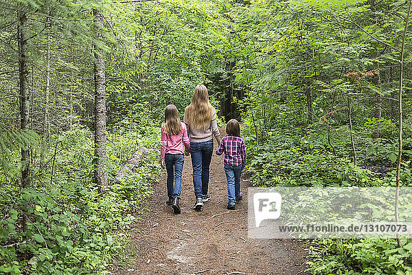Three sisters walking together and holding hands on a trail; Salmon Arm  British Columbia  Canada