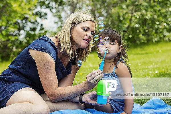 A beautiful young mother blowing bubbles with her daughter while sitting on a blanket in a city park during a warm sunny day; Edmonton  Alberta  Canada