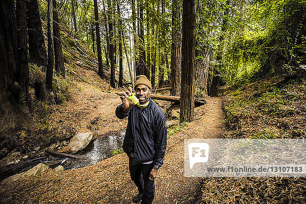 A man stands on a forest trail holding up an eaten apple to the camera  Julia Pfeiffer Burns State Park; California  United States of America