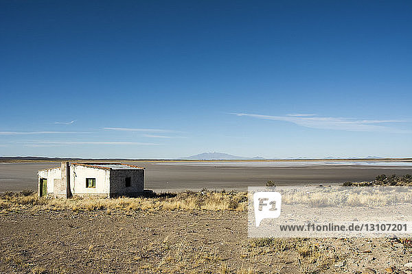 Weite Sicht auf ein trockenes Seebett mit einem Vulkan in der Ferne. Ein verlassenes weißes Gebäude ist im Vordergrund; San Rafael  Mendoza  Argentinien