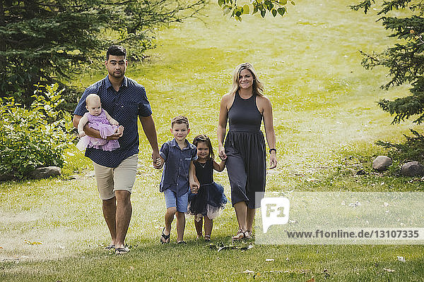 Eine Mutter und ein Vater in einer gemischtrassigen Ehe gehen mit ihren Kindern bei einem Familienausflug an einem warmen Herbsttag in einem Park spazieren  während ihr Sohn für die Kamera posiert; Edmonton  Alberta  Kanada