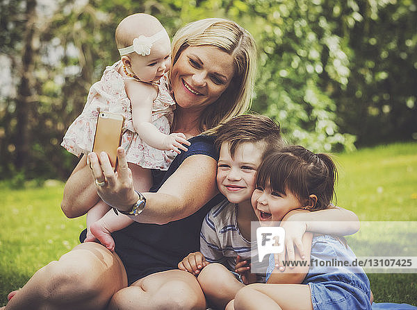 A young mother taking a self-portrait with her kids in a park with the image having a vintage effect applied; Edmonton  Alberta  Canada