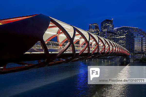 A red tunnel bridge across a river reflecting light at night with buildings in the background; Calgary Alberta Canada