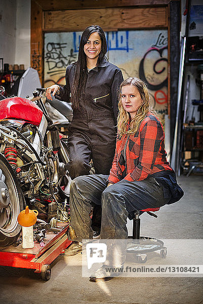 Portrait of confident female mechanics by bike in workshop