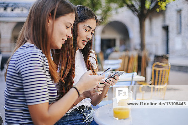 Freunde benutzen Mobiltelefone  während sie im Straßencafé sitzen