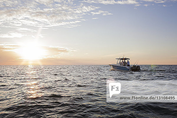 Männer und Jungen  die bei Sonnenuntergang auf einem Boot auf See gegen den Himmel fahren