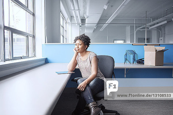 Nachdenkliche Geschäftsfrau schaut weg  während sie im Büro auf einem Stuhl sitzt