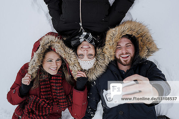 Hochwinkel-Freunde beim Selfie  während sie auf einem schneebedeckten Feld liegen
