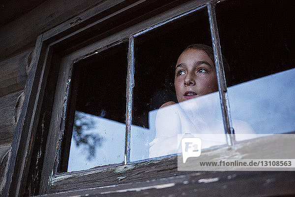 Niedrigwinkelansicht eines nachdenklichen Mädchens  das durch ein Fenster durch Glas schaut