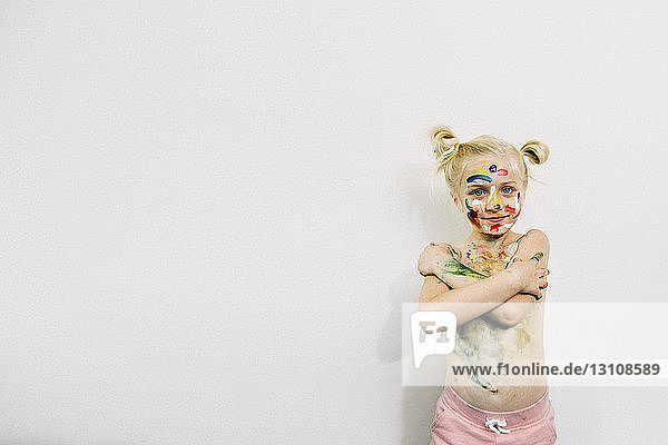 Cute girl covered in messy paint standing against white wall