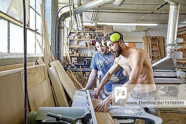 Carpenter guiding male coworker while standing in workshop