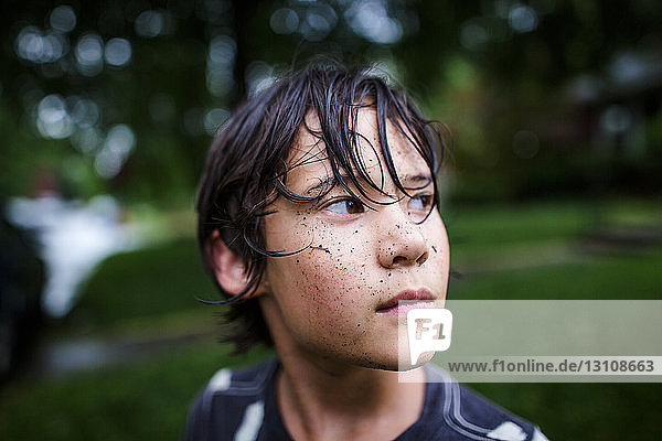 Nahaufnahme eines nachdenklichen Jungen mit schmutzigem Gesicht  der während der Regenzeit im Hof steht