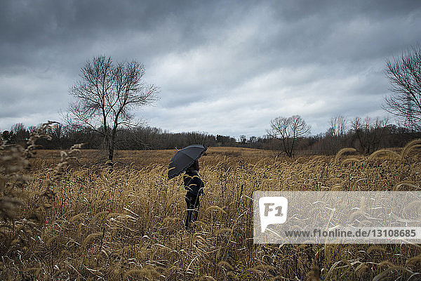 Teenage girl with umbrella standing on field against stormy clouds