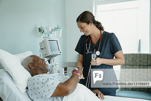 Lächelndes Händeschütteln der Krankenschwester mit einem älteren Patienten  der auf der Krankenhausstation auf dem Bett liegt
