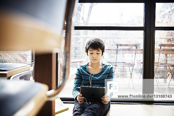 Junge benutzt digitales Tablett  während er zu Hause am Fenster sitzt
