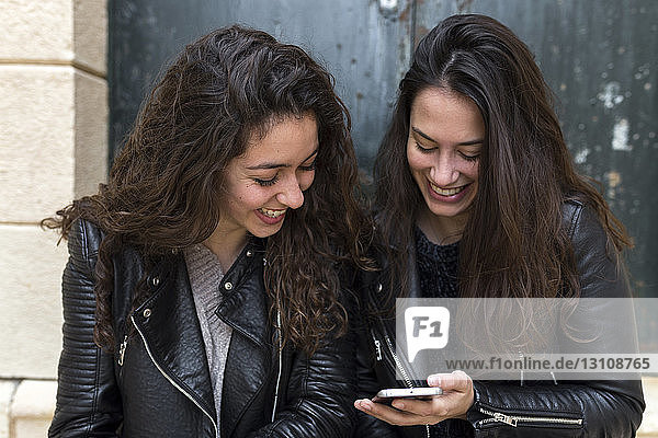 Glückliche Freunde  die an der Tür sitzend ein Mobiltelefon benutzen